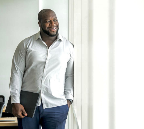 Devon Francis, Engineering Lab Technical Lead for Customer Experience at Victaulic, holds a laptop and looks out a window with a slight smile.